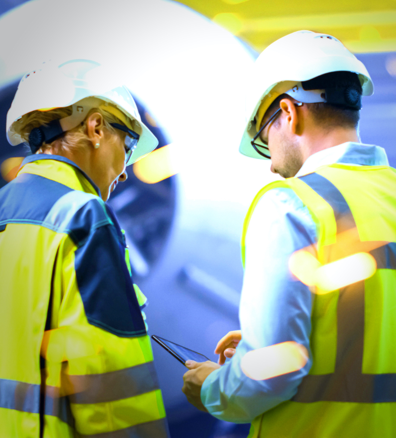 Man and woman in high-vis jackets and hard hats working at a facility